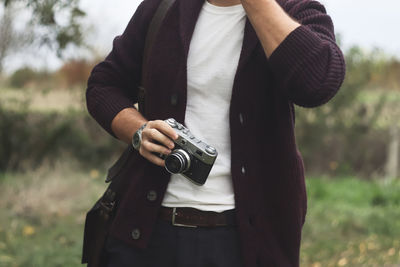 Midsection of man holding camera while standing outdoors