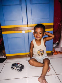 Portrait of smiling boy sitting on tiled floor at home