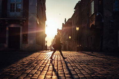 Side view of woman walking on footpath in city at sunset