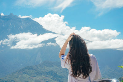 Rear view of woman looking at landscape against sky from mountain peak