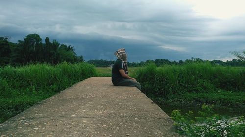 Side view of man sitting on field against sky