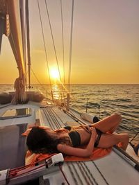 Woman lying on shore against sky during sunset