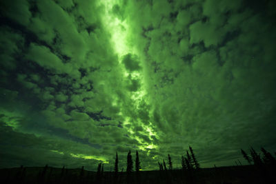 Silhouette landscape at tombstone territorial park against cloudy sky during aurora borealis