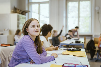 Portrait of smiling schoolgirl sitting at desk in classroom