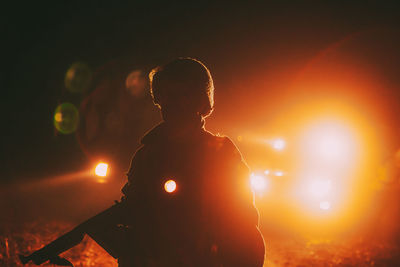 Rear view of silhouette man standing against sky at night