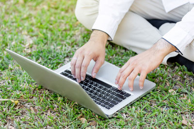 Low section of man using laptop on grassy land