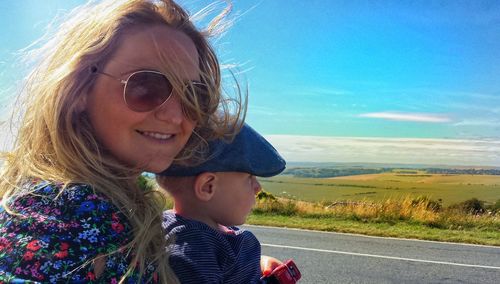 Portrait of mother carrying son at roadside against sky