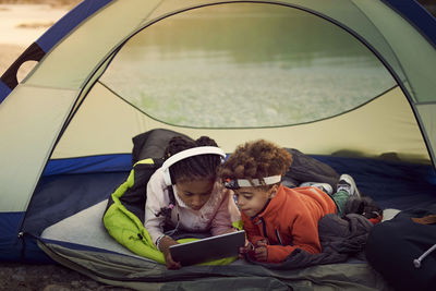 Siblings with digital tablet lying in tent