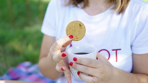 Midsection of woman holding biscuit and teat while sitting outdoors