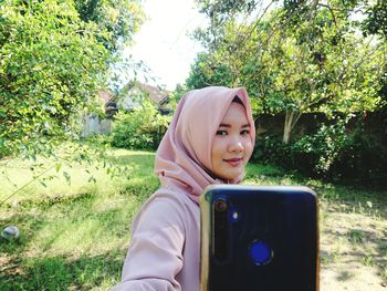 Smiling young woman doing selfie while standing at lawn