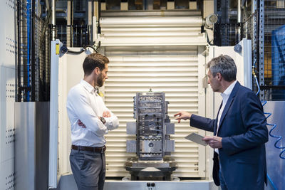 Businessmen during meeting with tablet, workpiece in production hall