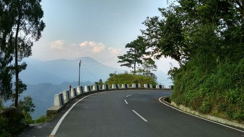 Empty road by trees against sky