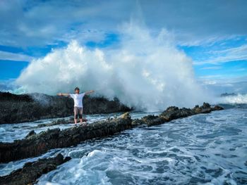 Man with arms outstretched standing on rock in against cloudy sky