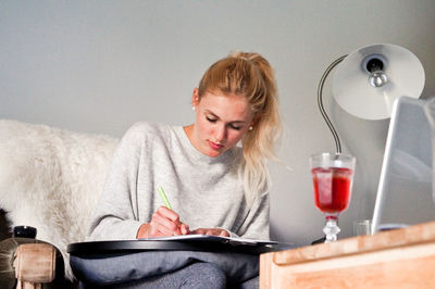 Young woman writing while sitting at home
