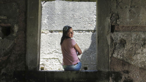 Rear view of smiling woman looking away while sitting on window sill