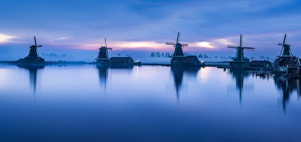 Windmills reflecting in water at sunset, creating a serene natural landscape