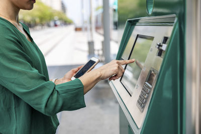 Woman with smart phone using ticket machine