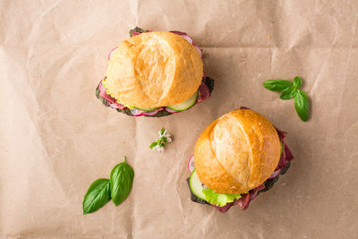 Ready-to-eat hamburgers with pastrami, cucumber, radish and herb on craft paper.