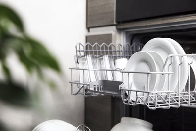 Front view of open dishwasher machine with clean utensils, cutlery inside. household domestic