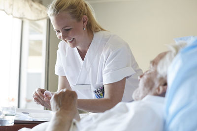 Happy female nurse giving cough syrup to senior man in hospital ward