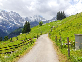 Road amidst green landscape and mountains against sky