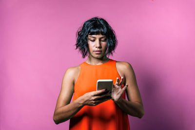 Young woman using phone while standing against pink background