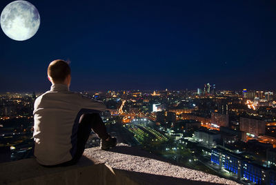 Rear view of man looking at illuminated city buildings