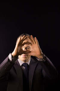 Portrait of businessman gesturing against black background