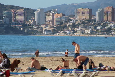 People at beach against city