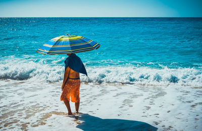 Man holding umbrella while standing at sea shore on sunny day