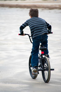 Rear view of boy cycling on sand at beach