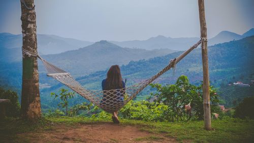 Rear view of woman looking at mountains while sitting on hammock 