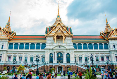 People in front of building against cloudy sky