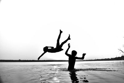 Silhouette boys enjoying at lake against clear sky