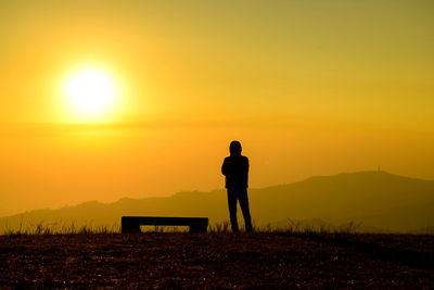 Silhouette man standing on field against sky during sunset