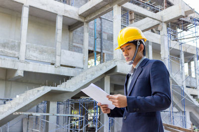 Engineer reading blueprint while standing at construction site