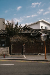 Man walking on road by buildings against sky