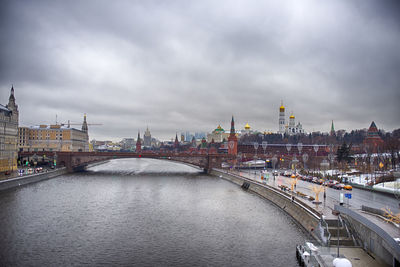 Bridge over river amidst buildings in city against sky