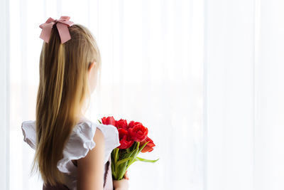 Woman holding red rose against white wall