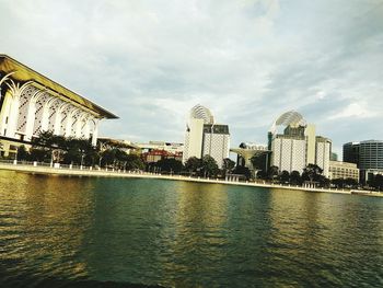 Buildings by river against sky in city