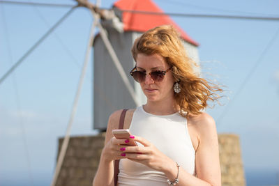 Woman in sunglasses using mobile phone against sky