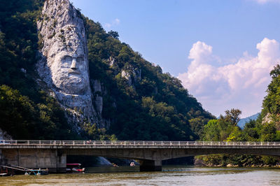 Decebalus carved on rock formation by river against sky