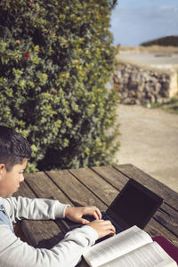 Young latin student, outdoors, using laptop sitting at a park