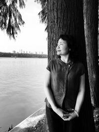 Thoughtful woman looking away while standing by tree trunk