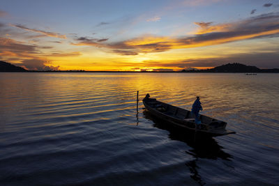 Fishing boat in lake against sky during sunset