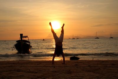 Full length of man practicing handstand at beach against sky during sunset
