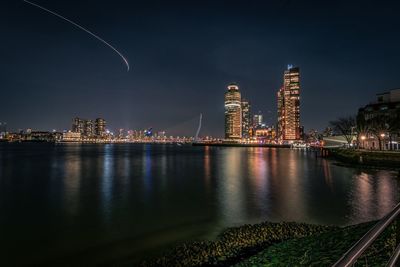 Illuminated buildings by river against sky at night