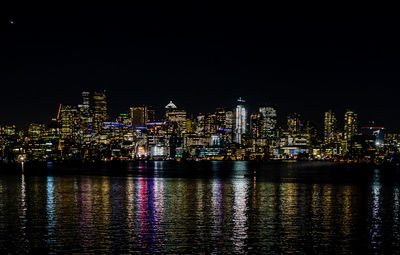 Illuminated buildings by river against sky at night