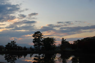 Silhouette trees by lake against sky during sunset