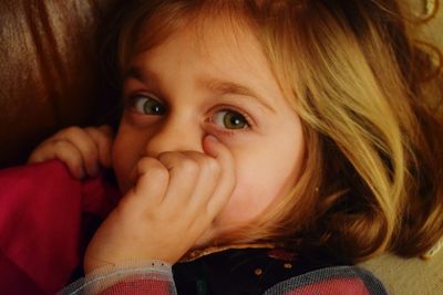 Close-up portrait of little girl sucking thumb at home